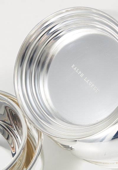 Sidabro spalvos metaliniai indai su lakuotais paviršiais, turintys grioveliais išpuoštas kraštus. Apačioje pažymėta "Ralph Lauren". Atspindinti tekstūra.