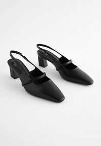 Tacones negros de salón con puntera puntiaguda y tacón cuadrado. Fabricados en cuero suave con una correa delgada en la parte superior.
