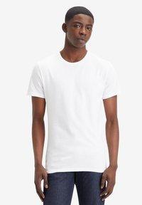 Tricou alb cu mânecă scurtă, cu guler rotund, realizat din țesătură de bumbac moale, având un design simplu, fără modele sau grafice.