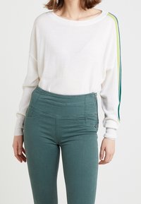 Maglietta bianca a maniche lunghe con strisce laterali verdi e gialle abbinata a pantaloni teal a vita alta con tasca con zip e design strutturato.