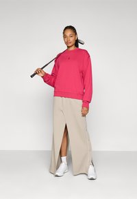 Sweatshirt rosa com decote redondo, combinado com uma saia maxi bege com uma fenda frontal e detalhes em botões, complementado por ténis brancos.