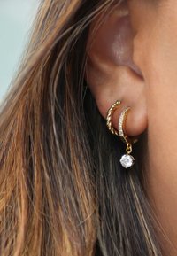 Les boucles d'oreilles en or ont un design torsadé avec une goutte en cristal. La surface est polie et les boucles d'oreilles mettent en valeur un accent scintillant.