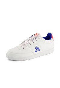 Sneaker bianco in pelle con accenti blu e rossi, suola in gomma testurizzata e logo distintivo. Presenta lacci a contrasto e dettagli perforati.