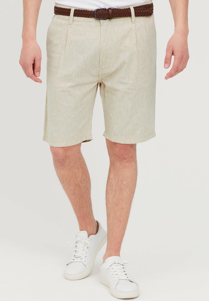 Beige linnedragt shorts med en afslappet pasform, der har en tekstureret overflade og lommer, parret med et brunt vævet bælte og hvide sneakers.