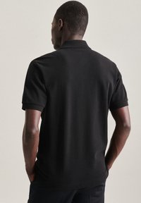 Polo shirt nera realizzata in cotone, con colletto classico e maniche corte. Texture liscia e design semplice e pulito.