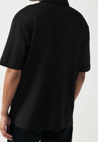 Musta lyhythihainen poolopaita, joka on valmistettu puuvillasta. Paidassa on klassinen kaulus ja rento malli, jonka pinnassa on sileä rakenne ja siistit reunat.