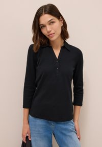 Polo noir à manches longues avec un col en V, trois boutons à l'avant et un ourlet droit, associé à un jean bleu clair.