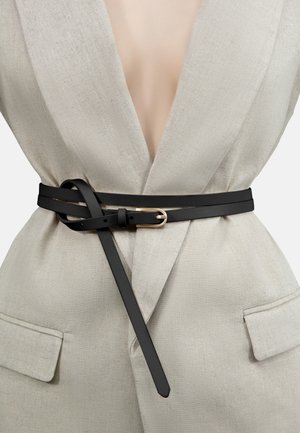 Black leather belt with a double loop design and gold-tone buckle, worn over a light beige linen outfit. Smooth texture and minimalist style.