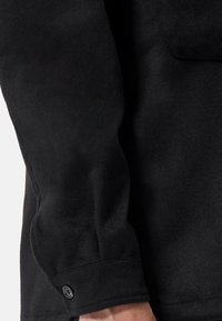 Zwarte fleece jack met een zachte textuur, lange mouwen en een knoopdetail aan de manchetten. Eenvoudig, strak ontwerp.