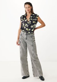 Sort blomsterbluse med grønne og hvide mønstre, parret med højtaljede, lysegrå wide-leg jeans med kontrastsyninger. Sko med sorte prikker.
