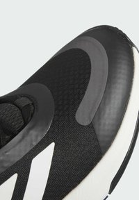Zwarte sportieve schoen met een mesh bovenwerk, gladde accenten en een kenmerkend wit logo. Gelaagd en gestroomlijnd ontwerp met een ronde neus.