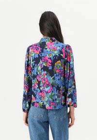 Blouse florale avec un fond bleu marine, ornée de fleurs vibrantes roses, bleues et vertes, manches bouffantes et col. Associée à un jean taille haute.