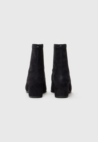 Black suede ankle boots with a smooth texture and rounded toe. Features a squared heel and a logo accent at the back.
