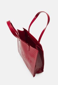 Rode croco-embossed tote bag met twee handvatten, open bovenkant en binnenzijde met ritsvak. Glanzende textuur met gegraveerd logo detail aan de voorkant.