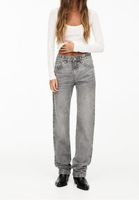 Szare dżinsy z denimu o luźnym kroju, z wysokim stanem, pięcioma kieszeniami oraz subtelną wyblakłą fakturą. W zestawieniu z białą bluzką z długim rękawem. Czarne botki za kostkę.