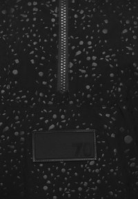 Svart tyg med spridda glänsande grå fläckar, en vertikal dragkedja i mitten och ett sydd rektangulärt märke som är märkt "70" nära botten.