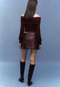 Burgunderfarbener schulterfreier Pullover, figurbetonender Leder-Minirock und kniehohe schwarze Stiefel mit roten Absätzen. Glatte Textur, körperbetontes Design.