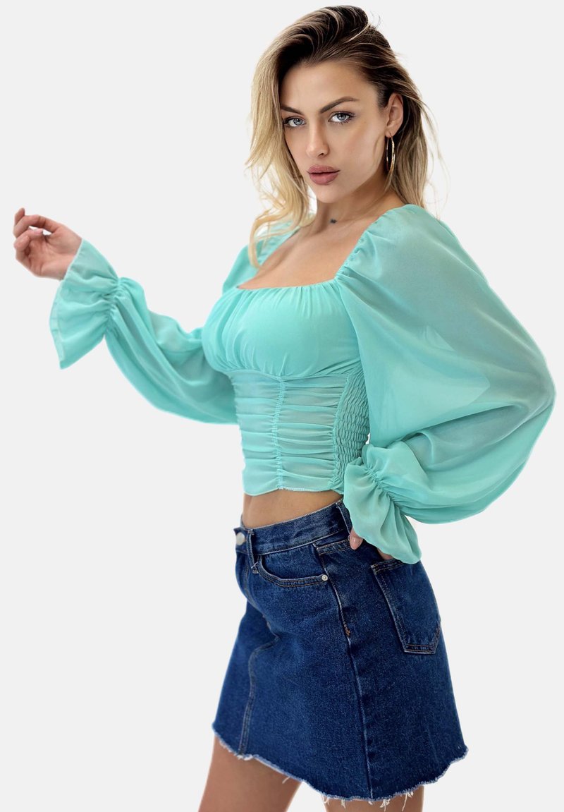 Top azzurro chiaro con maniche a sbuffo e dettagli arricciati, abbinato a una mini gonna in denim scuro con orlo sfilacciato e tasche laterali.