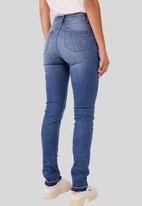 Hautenge Jeans aus mittelblauem Denim, hochgeschnittenes Design, mit Gesäßtaschen und dekorativen Nähten sowie einer glatten, leicht abgenutzten Textur.