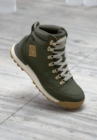 Botte de randonnée verte avec une finition texturée, semelle crème, lacets argentés et logo en patch. Dotée d'un excellent maintien de la cheville et d'œillets métalliques.