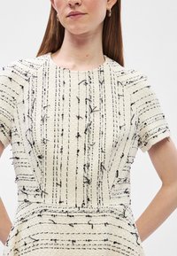 Krēmpu kleita ar melnām tekstūrētām līnijām, īsām piedurknēm un pieguļošu jostu. Ir izvirzītas šuves un apaļa kakla izgriezums.