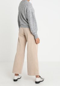 Grå, texturerad tröja med en lös passform, kombinerad med ljusbeiga byxor med vida ben. Skorna har svarta och vita kontrastdetaljer.