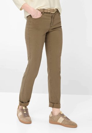 Persona che indossa pantaloni kaki con orli arrotolati, cintura color sabbia, maglia a maniche lunghe beige e sneakers beige con lacci e suole marrone chiaro.