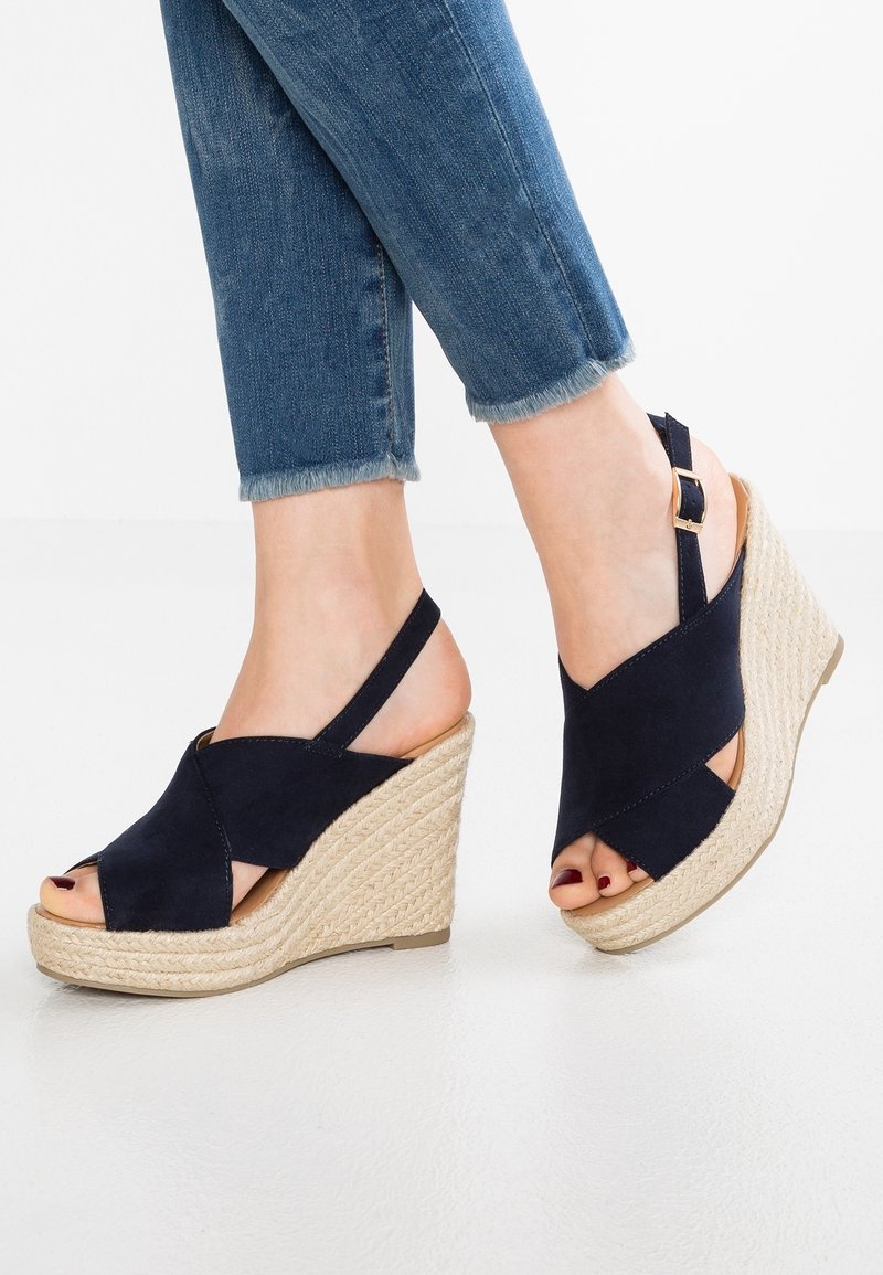 Mörkblå mocka kilklacksandaler med korsade remmar, öppen tå och vävd jute-baserad sula. Justeras med en spännrämsrem bak.