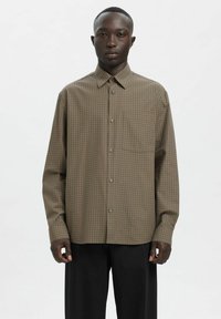 Brązowa koszula w kratę na guziki z kołnierzykiem, długimi rękawami i pojedynczą kieszenią na piersi. Wykonana z lekkiej tkaniny o luźnym kroju.