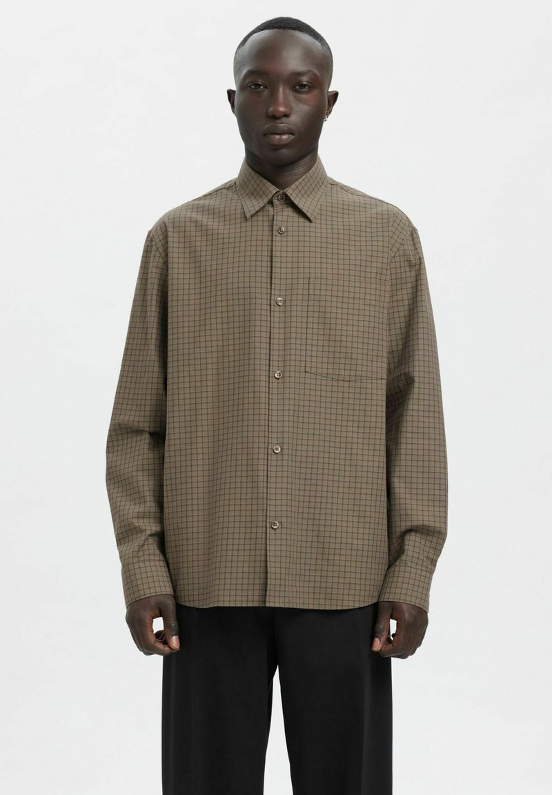 Brązowa koszula w kratę na guziki z kołnierzykiem, długimi rękawami i pojedynczą kieszenią na piersi. Wykonana z lekkiej tkaniny o luźnym kroju.