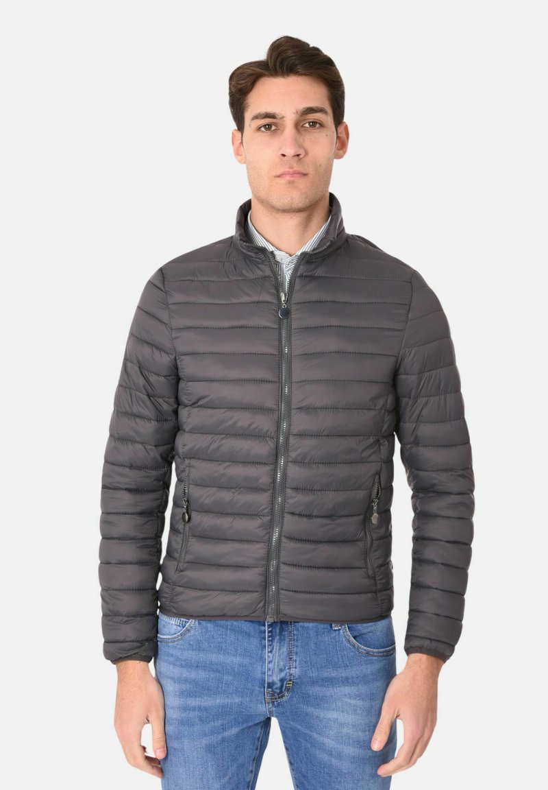 Giacca grigia imbottita con collo rialzato, motivo a righe orizzontali, chiusura con zip frontale e tasche laterali, abbinata a jeans blu.