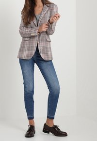Blazer à carreaux dans des nuances de beige et marron, associé à un t-shirt gris, un jean skinny bleu et des chaussures à lacets marron foncé.