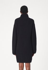 Robe pull en tricot noir avec un col montant, des manches longues et une coupe ample, présentant une texture côtelée sur l'ensemble.