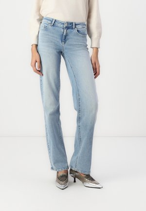 Jean bleu clair taille haute et coupe droite, porté avec des chaussures argentées à bout pointu et talons kitten, ainsi qu’un top crème à manches longues.