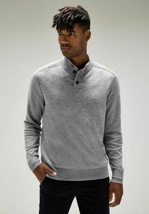 Suéter de punto gris con un cuello alto, tapeta de dos botones, puños y dobladillo acanalados. Textura suave con sutiles variaciones en el color.