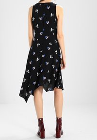 Vestido negro sin mangas con estampado floral en azul, blanco y rosa. Presenta un dobladillo asimétrico y una tela suave y ligera. Botines rojos hasta el tobillo.