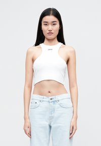 Top de tanque blanco recortado con cuello alto y diseño sin mangas, con la palabra "OFF" impresa en negro. Combinado con jeans de mezclilla azul claro.