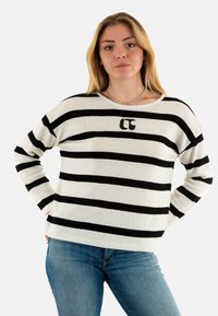 Maglione a righe in bianco e nero, con colletto rotondo, maniche lunghe e un piccolo logo sul petto. Tessuto morbido e lavorato a maglia.