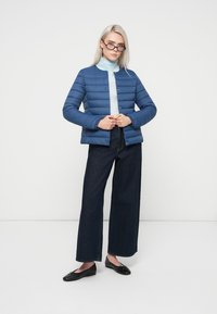 Modrá vypchatá bunda s horizontálnym prešívaním a zapínaním na gombíky, nosená cez svetlomodrý rolák. Skombinovaná s tmavými džínsy so širokými nohavicami a čiernymi balerínkami.