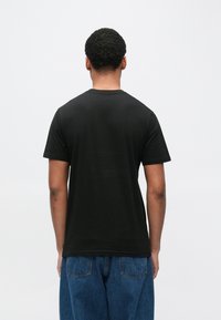 Sort bomuld T-shirt med rund hals og korte ærmer, set bagfra, kombineret med blå denimjeans, der har en afslappet pasform.