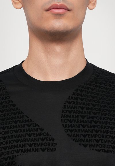 Melnas īsām piedurknēm T-krekls ar strukturētu zīmola nosaukuma "Emporio Armani" rakstu glancētā apdarei. Apaļš dekoltē.
