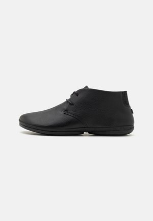 Black leather ankle boots with a smooth finish, round toe, minimalistic design, and lace-up front, featuring a flexible outsole.