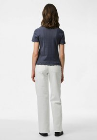 Kortärmad marinblå topp med texturerad yta och vågig fåll, kombinerad med vita raka jeans och svarta skor.