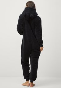 Zwart harig fleece onesie met een capuchon, voorzien van berenoren, lange mouwen en geribde boorden. Zachte textuur met een ontspannen pasvorm.