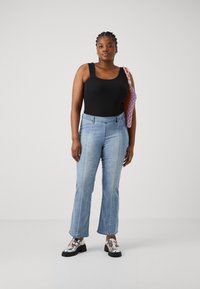 Črna brezrokavnica v kombinaciji s svetlo modrimi bell-bottom jeans hlačami. Obute so bleščeče srebrne platform cestne čevlje in multikolor torba iz tkanine.