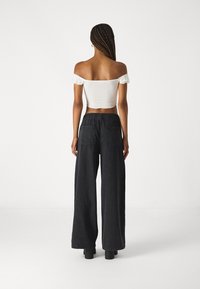 Hvit av-shoulder crop topp med volanger, kombinert med mørke vidde benbukser med elastisk midje og baklommer.