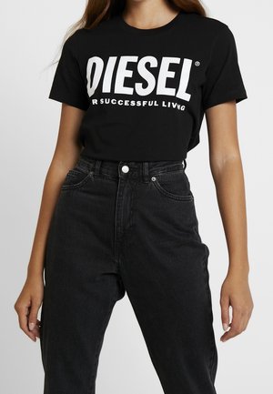 Kobieta ubrana w czarny t-shirt Diesel z białym napisem oraz czarne dżinsy z wysokim stanem na jednolitym jasnym tle.