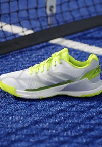 White and neon green sports shoe on a blue textured court surface near a black net with white boundary lines.