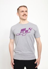 Šedé tričko s krátkým rukávem s fialovým grafickým designem abstraktních tvarů a linií na přední straně. Hladká bavlněná textilie.