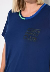 Camiseta de color azul marino con mangas cortas, con un escote redondo con acento verde y un gráfico de texto que dice "CLUB DE ENERGÍA INFINITA" en negro.